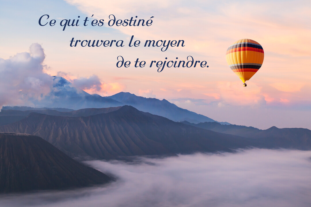 Une montgolfière jaune et rouge flotte au-dessus d'un paysage montagneux enveloppé de brume, sous un ciel de lever de soleil.