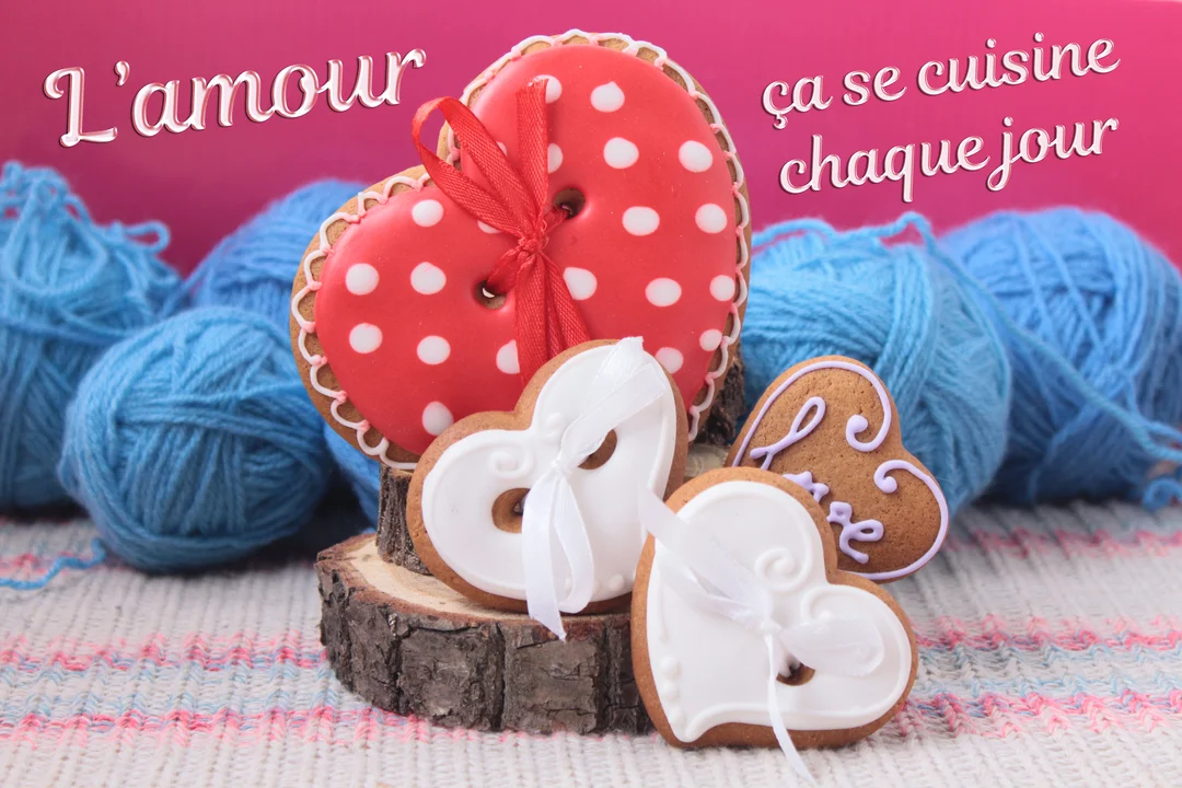 Une composition de biscuits en pain d'épice en forme de cœur, décorés et posés sur une rondelle de bois devant des pelotes de laine bleues.