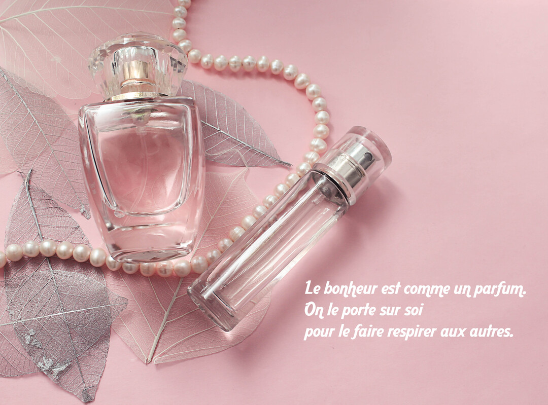 Une composition élégante de flacons de parfum et d'un collier de perles sur un fond rose, illustrant une citation sur le bonheur.
