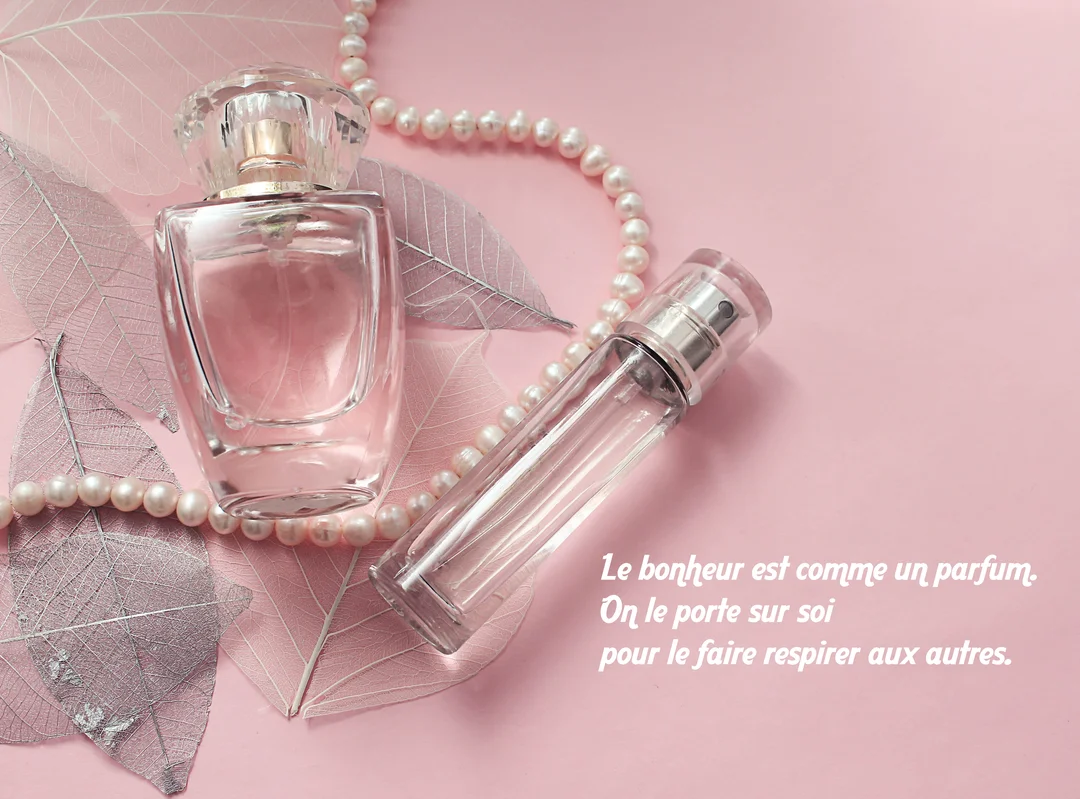 Une composition élégante de flacons de parfum et d'un collier de perles sur un fond rose, illustrant une citation sur le bonheur.