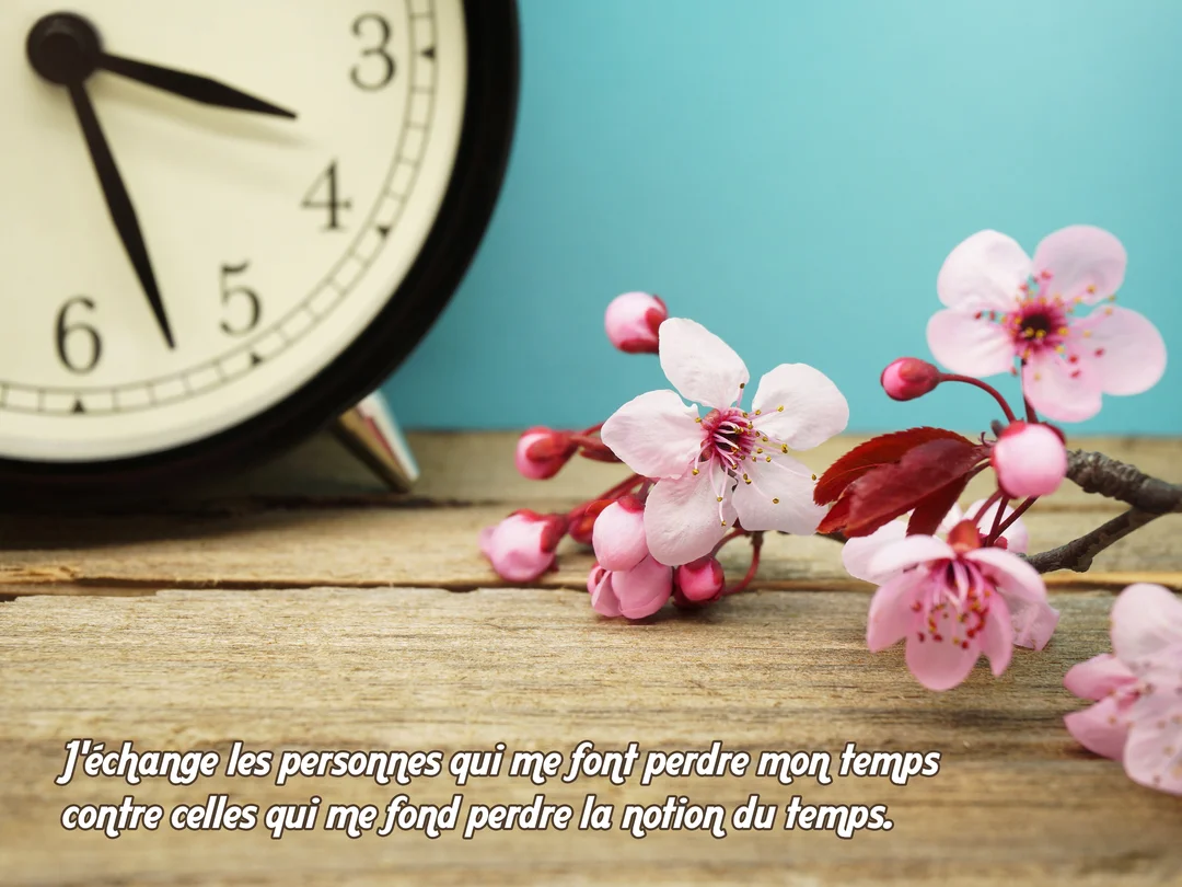 Au premier plan, une branche de cerisier en fleurs roses repose sur une table en bois, avec une horloge vintage floue en arrière-plan.