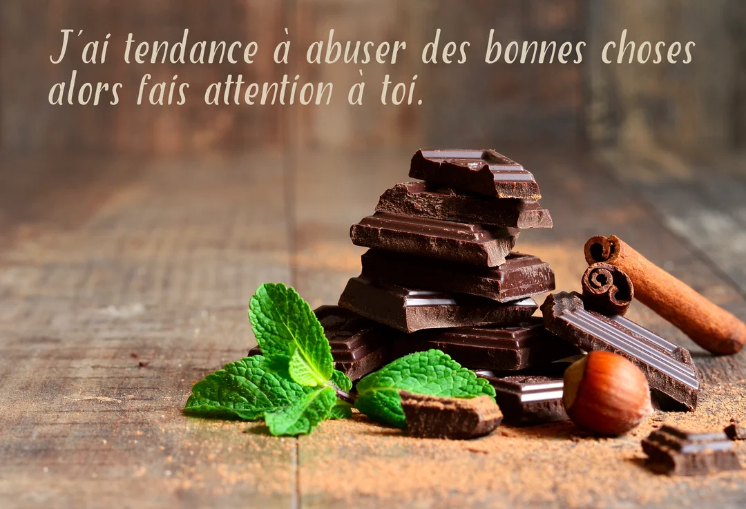 Une pile de carrés de chocolat noir est posée sur une table en bois, accompagnée de menthe fraîche, d'une noisette et de bâtons de cannelle.