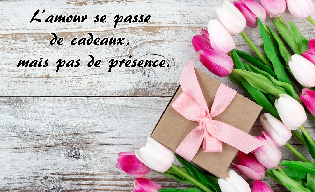 Une citation sur l'amour est écrite sur un fond en bois blanc à côté d'un bouquet de tulipes roses et d'une boîte cadeau.