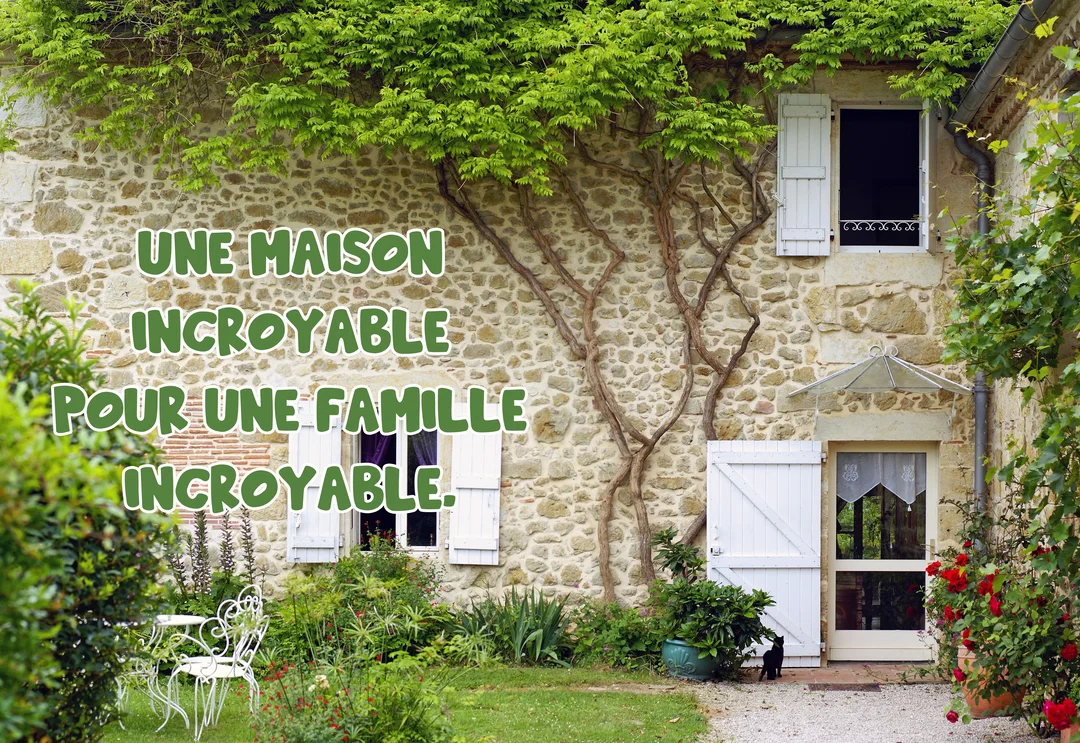 Une façade de maison en pierre avec une glycine, un jardin verdoyant, des volets blancs, et un chat noir près de la porte.