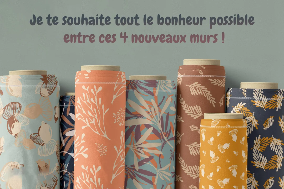 Plusieurs rouleaux de papier peint aux motifs naturels et colorés sont posés devant un mur vert sauge, surmontés d'un message de vœux.