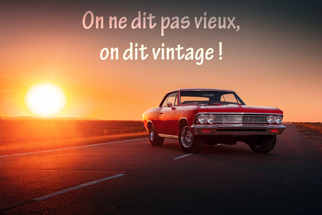 Une voiture de collection rouge est garée sur le bas-côté d'une route déserte, face à un flamboyant coucher de soleil à l'horizon.