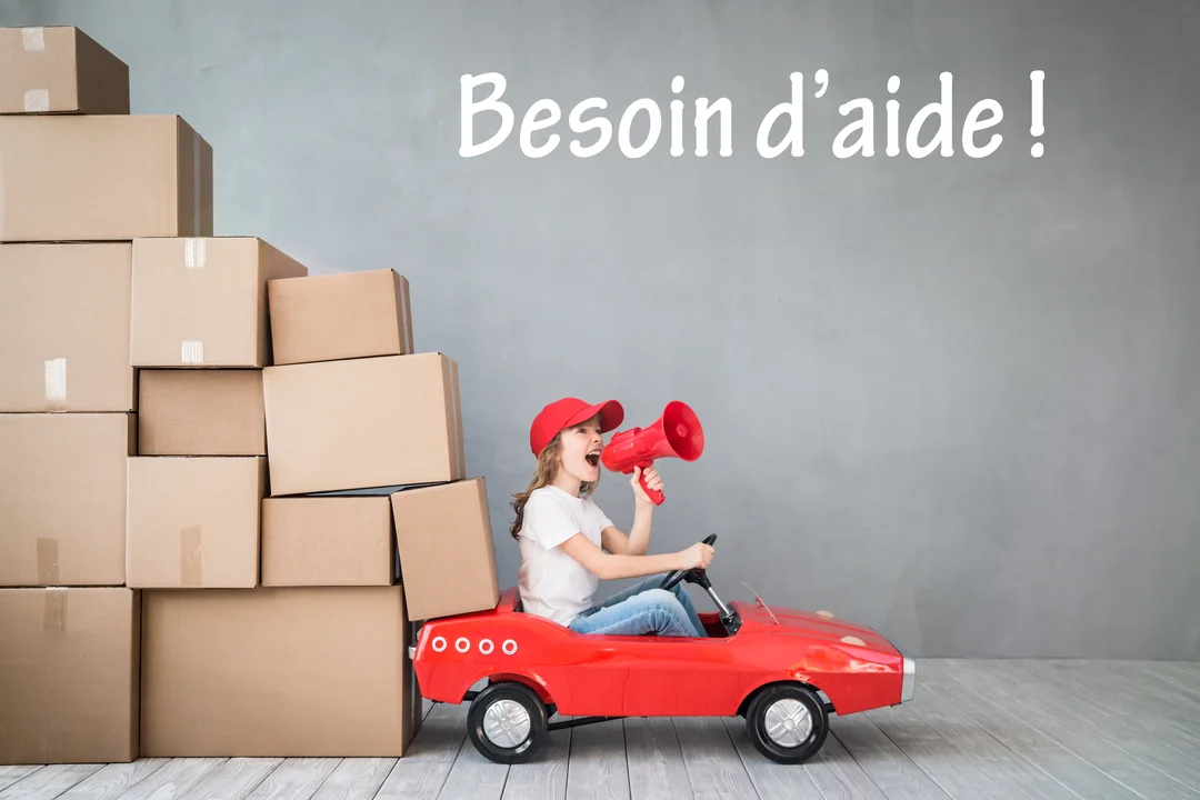 Une jeune fille dans une voiture jouet rouge crie dans un mégaphone, à côté d'une haute pile de cartons de déménagement.