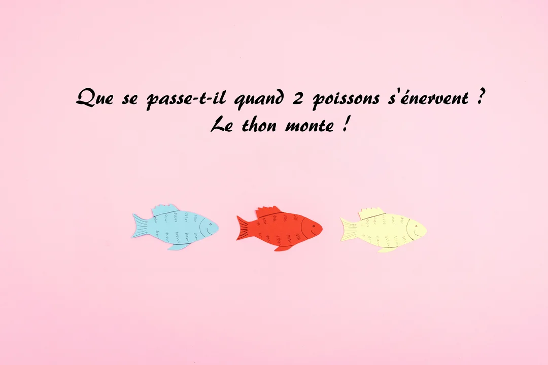 Sur un fond rose, une blague sur le poisson d'avril est écrite au-dessus de trois poissons en papier coloré alignés horizontalement.