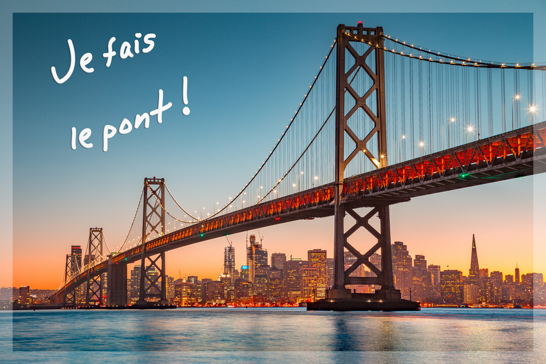 Un grand pont suspendu illuminé enjambe une baie, avec une ligne d'horizon urbaine scintillante sous un ciel crépusculaire bleu et orange.