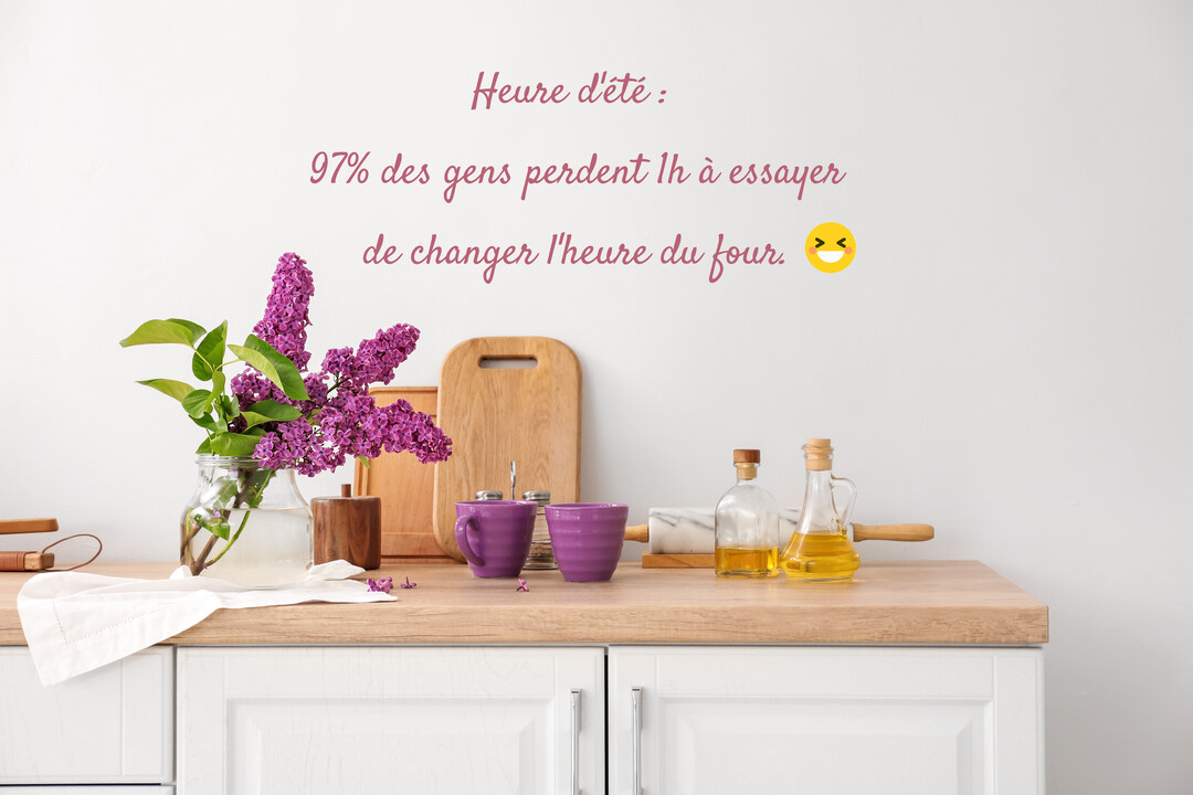 Sur un plan de travail de cuisine en bois, un bouquet de lilas violet dans un vase côtoie des tasses et des bouteilles d'huile.