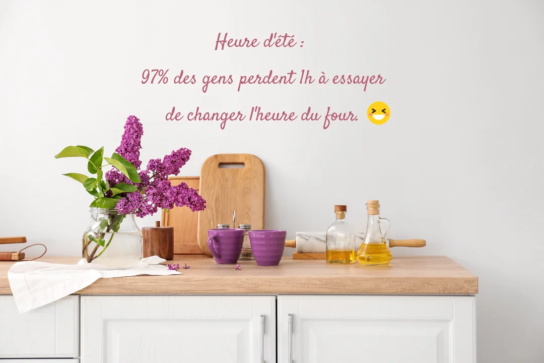 Sur un plan de travail de cuisine en bois, un bouquet de lilas violet dans un vase côtoie des tasses et des bouteilles d'huile.