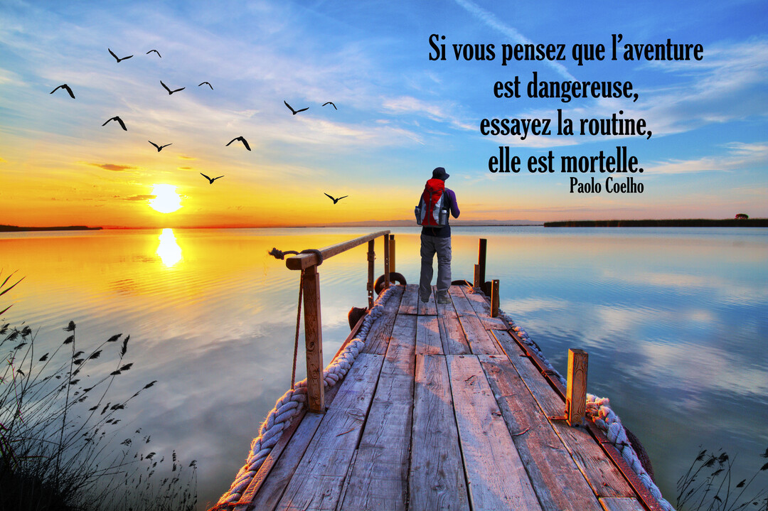 Un homme avec un sac à dos se tient sur un ponton en bois, contemplant un lever de soleil éclatant sur un lac calme.