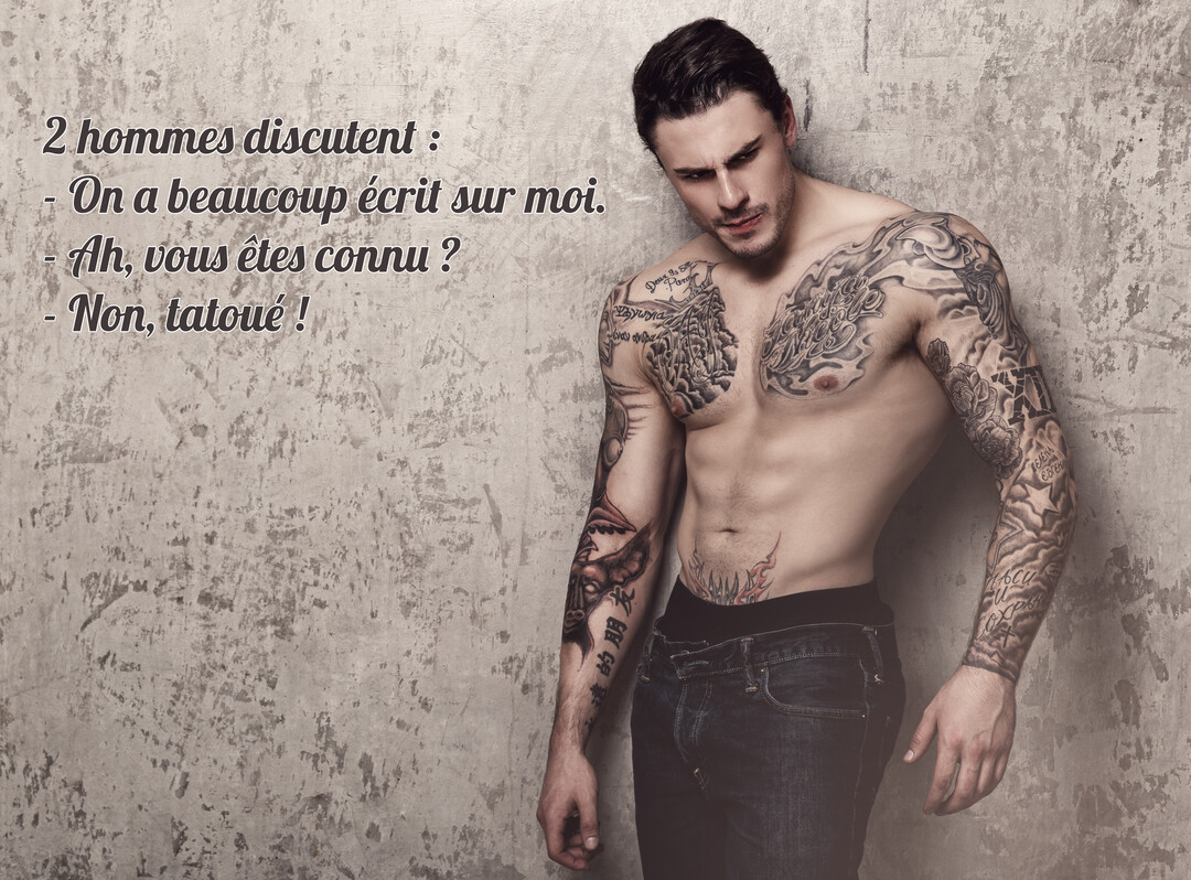 Un jeune homme musclé au torse nu, couvert de tatouages en noir et gris, regarde vers le bas avec une expression intense.