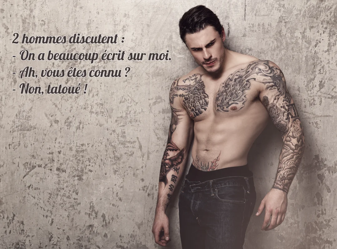 Un jeune homme musclé au torse nu, couvert de tatouages en noir et gris, regarde vers le bas avec une expression intense.