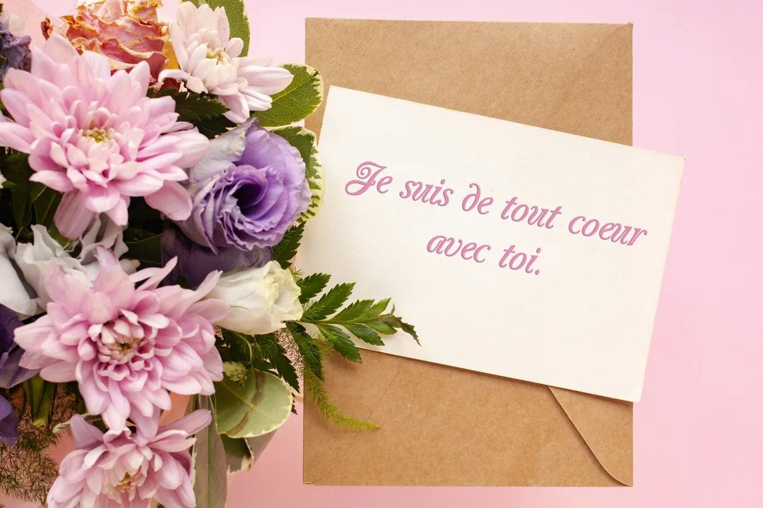 Un bouquet de fleurs roses et violettes est posé à côté d'une carte sur fond rose, avec un message de soutien manuscrit.