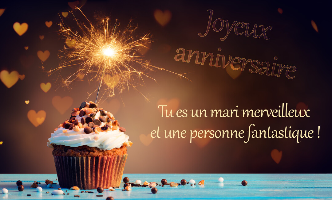 Un cupcake festif surmonté d'un cierge magique allumé, posé sur une table bleue, avec un message d'anniversaire pour un mari.