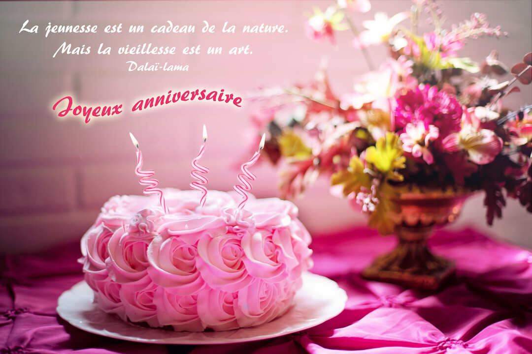 Une photographie d'un gâteau d'anniversaire rose avec des bougies, posé sur une nappe fuchsia, à côté d'un bouquet de fleurs colorées.