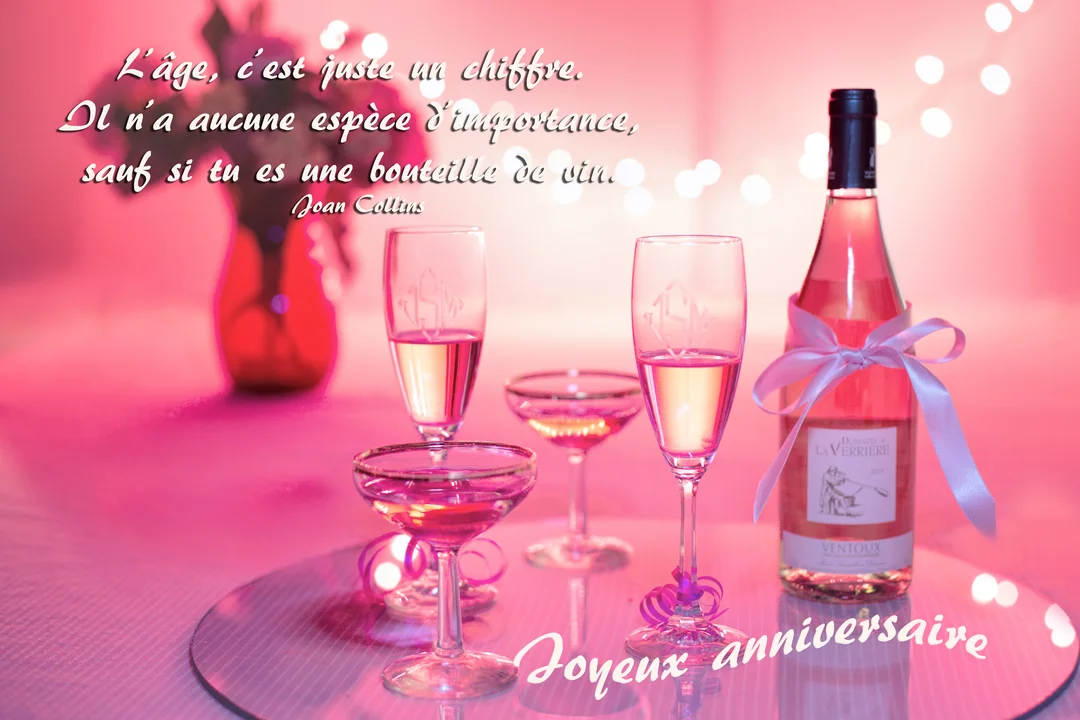 Une scène festive d'anniversaire avec une bouteille et des verres de vin rosé sur fond rose lumineux et la mention 'Joyeux anniversaire'.