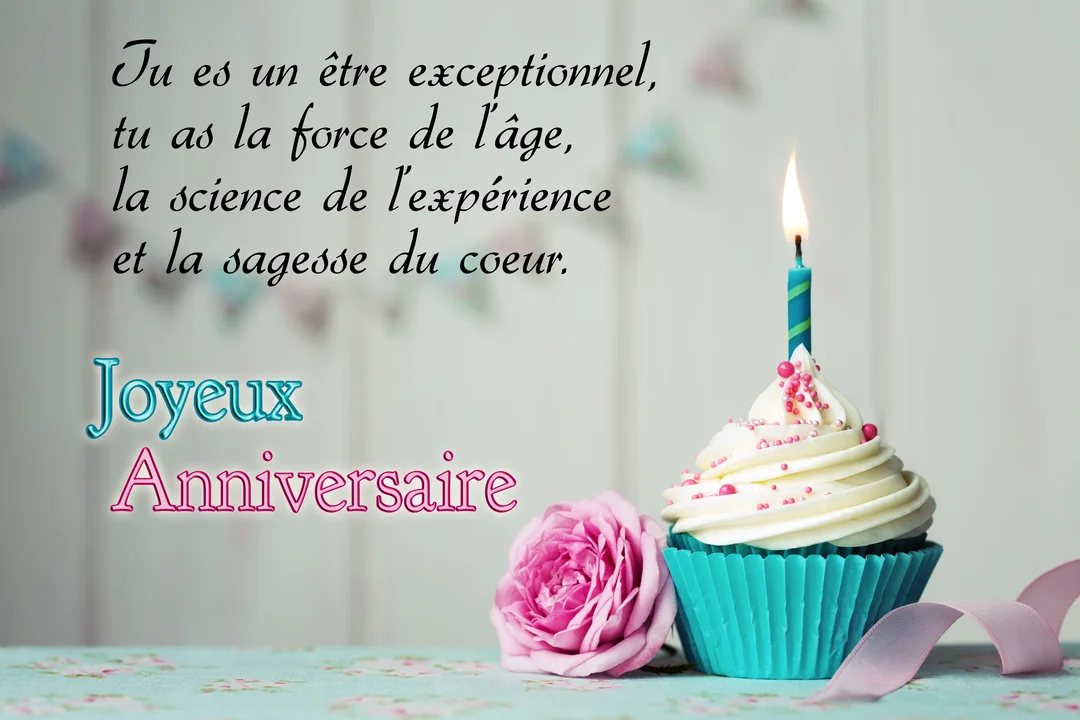 Un cupcake dans une caissette turquoise avec une bougie allumée, posé sur une table à côté d'une jolie rose de couleur rose.