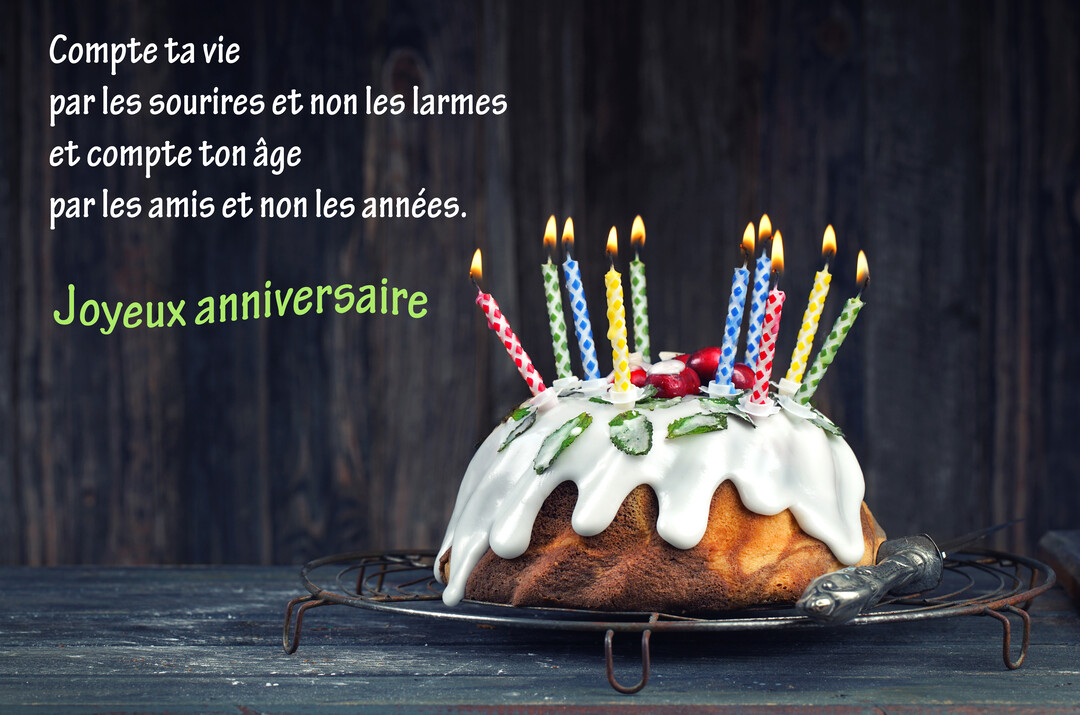 Un gâteau d'anniversaire en forme de couronne, nappé de glaçage blanc et garni de bougies colorées allumées, posé sur une grille rustique.