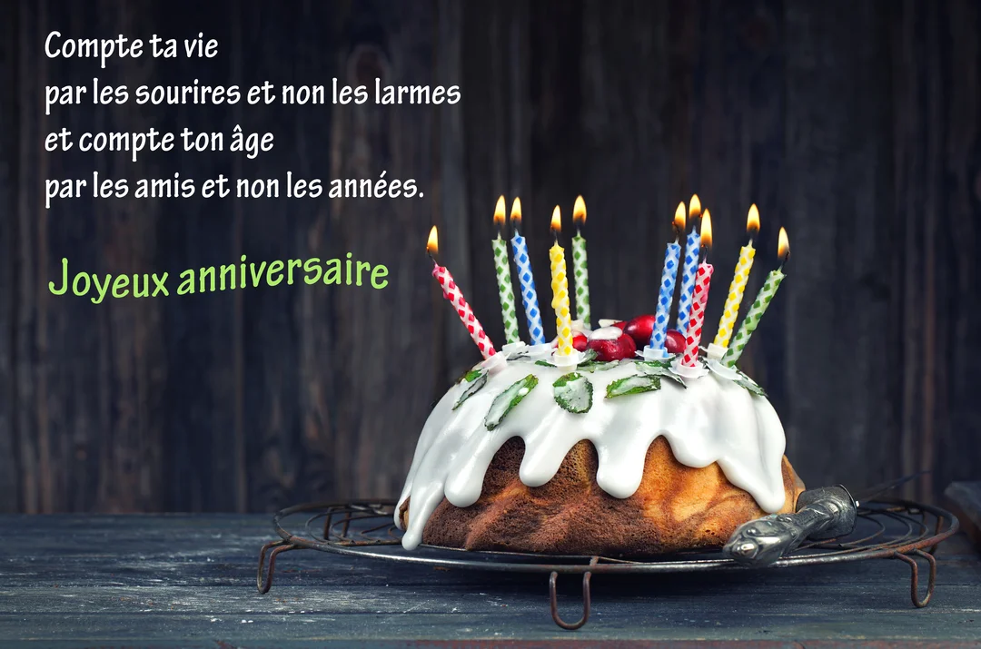 Un gâteau d'anniversaire en forme de couronne, nappé de glaçage blanc et garni de bougies colorées allumées, posé sur une grille rustique.