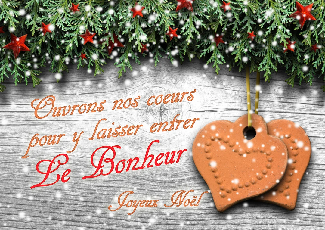 Deux cœurs en terre cuite suspendus à une guirlande de sapin avec des étoiles rouges, sur un fond en bois blanc enneigé.