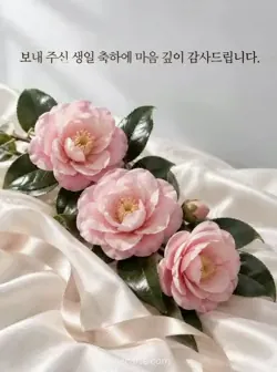접힌 아이보리색 비단 위에 연분홍 동백 세 송이와 짙은 잎, 샴페인색 리본이 놓인 정중한 생일 감사 카드