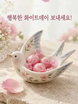 모래빛 돌 위의 제비 모양 도자기 접시에 분홍 사탕 세 개가 담겨 있고, 옆에는 분홍 꽃잎이 놓여 있어요. 위쪽에는 행복한 화이트데이를 바라는 인사가 있어요.